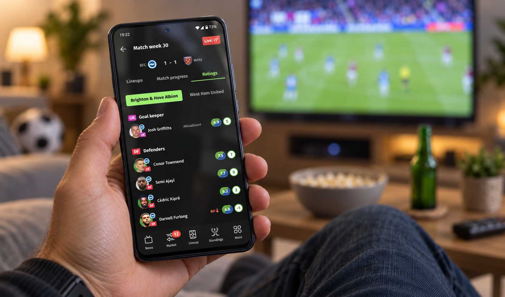 A user checking Comunio live player ratings on their phone while watching a match on TV